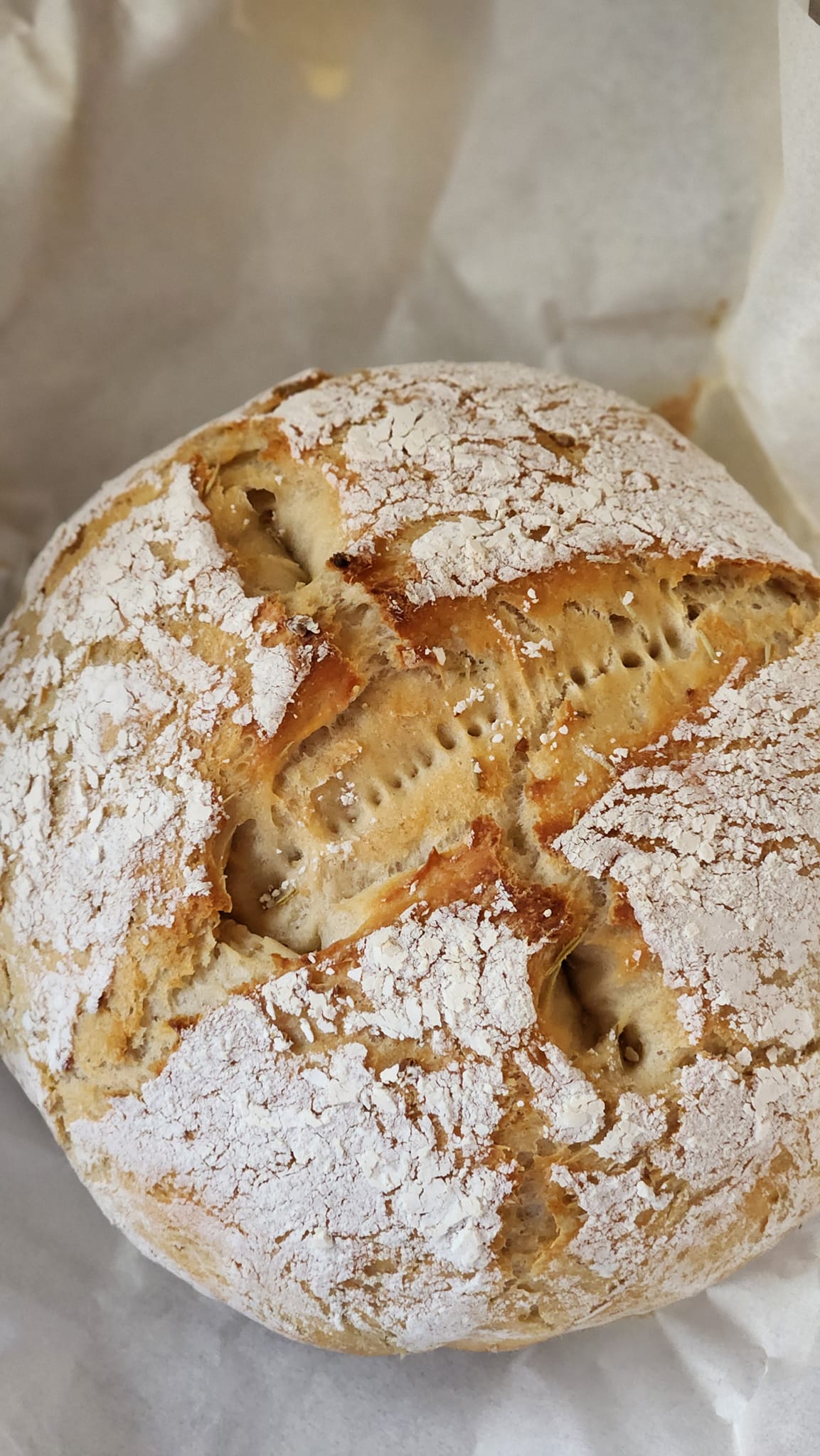 481825275_530966253362938_158489850625660651_n Artisan bread with a crusty exterior and flour dusting, showcasing its rustic texture and golden-brown color, placed on parchment paper.
