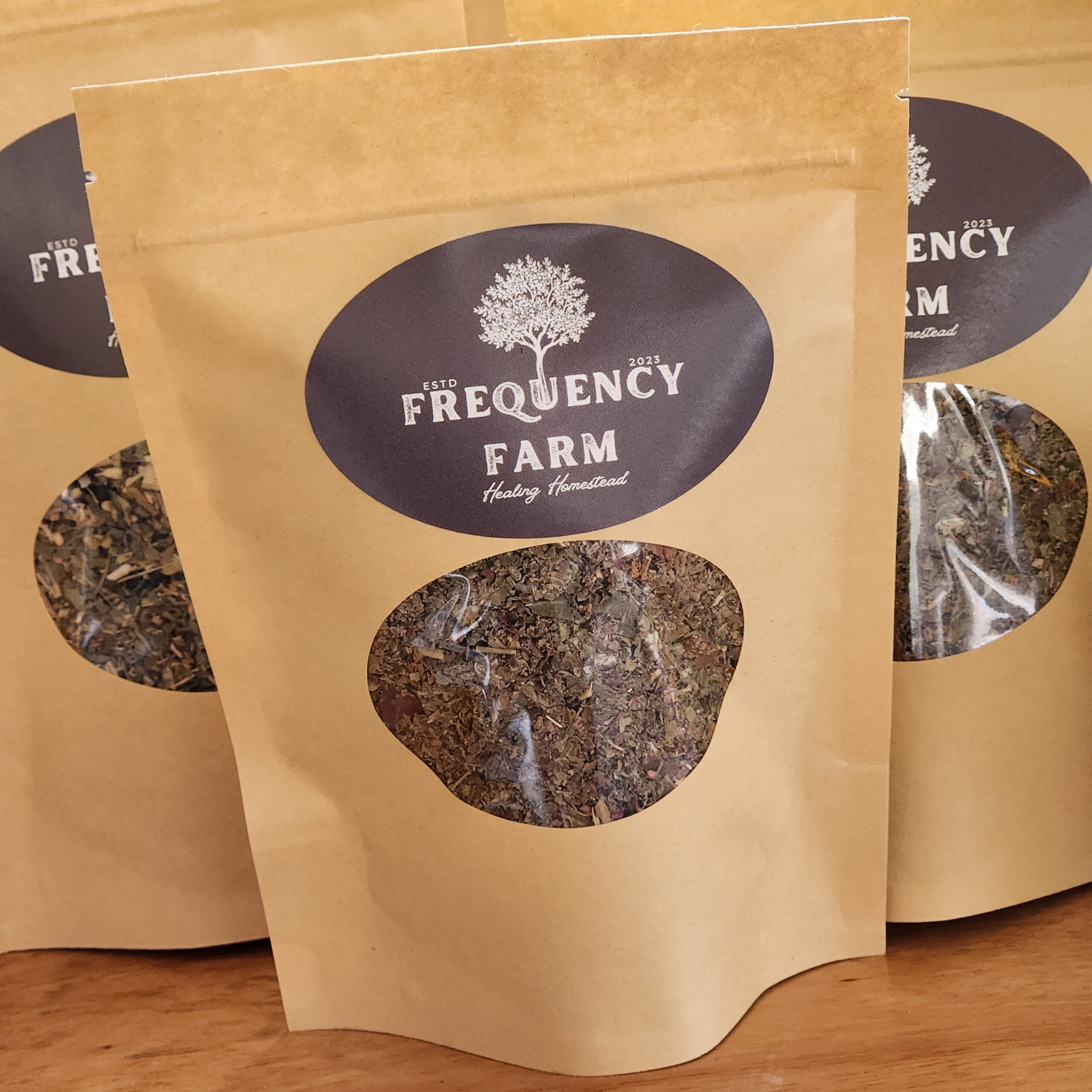 Caron Parker - 20230822_141042 Brown paper bags of dried herbs from Frequency Farm, featuring a clear window to display the contents and a logo emphasizing the brand's focus on healing and natural products.